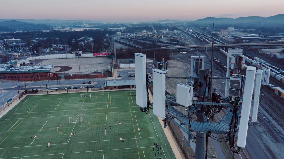 A cell tower rising over a suburban field at dusk.