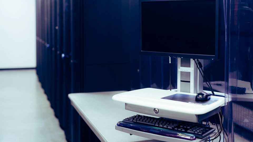A computer workstation positioned beside rows of server racks.